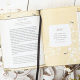 Open book with a page labeled 'July' on a decorative surface with plants and a cup.