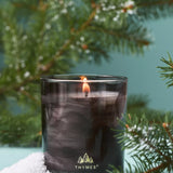 Thymes candle in a glass container with a Christmas tree branch in the background
