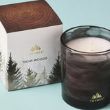 Thymes Noir Woods candle and packaging on a light blue background
