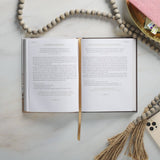 Open book with a gold bookmark on a marble surface, surrounded by decorative items.