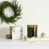 Festive arrangement with a green candle, box labeled 'Frasier Fir', and decorative wreath on a white surface.