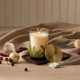Candle with a nature-themed design on a wooden tray with decorative items.