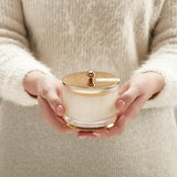 Person holding a white container with a gold lid against a neutral background