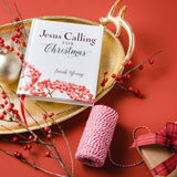 Book titled 'Jesus Calling for Christmas' by Sarah Young on a decorative tray with red berries and a gift, against a red background.