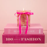 Candle with a pink ribbon on top of two pink books against a light pink background
