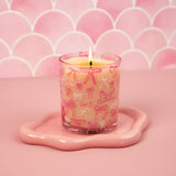 Candle in a glass holder with pink bow design on a pink background