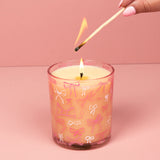 Candle with bow pattern being lit with a match against a pink background