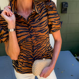 Woman wearing a tiger print shirt and holding a clutch in front of a building.
