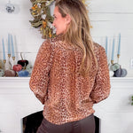 Person wearing a leopard print top in front of a decorated fireplace.