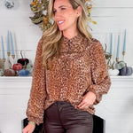 Woman wearing a leopard print blouse standing in front of a decorated fireplace.