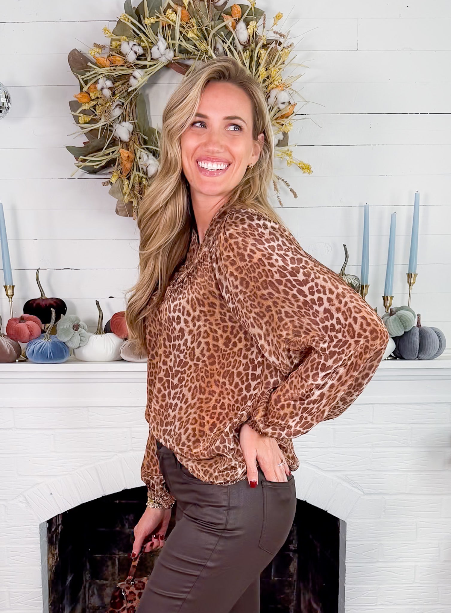 Woman wearing a leopard print blouse in front of a decorated fireplace.