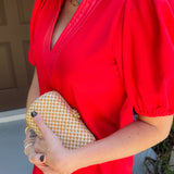 Person wearing a red dress holding a gold clutch against a neutral background