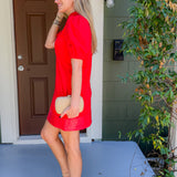 Woman in a red dress standing on a porch with a plant and door in the background