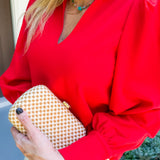 Person wearing a red blouse holding a gold clutch with a blurred background