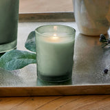 Green candle in a glass holder on a wooden surface with decorative elements.