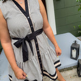 Woman wearing a black and white striped dress with a belt, standing outdoors.