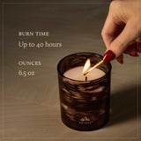 Candle being lit with text about burn time and ounces, on a neutral background.