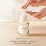 Hand holding a bottle of Thymes Frasier Fir hand soap with a neutral background
