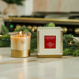 Votivo Red Currant candle and its packaging on a decorative surface with greenery.