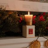 Votive candle in a decorative box on a mantelpiece with Christmas decorations.