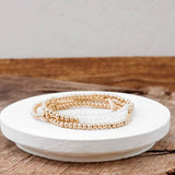 A stack of gold-tone glass bead bracelets on a white plate, with a wooden surface in the background.