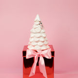 White ceramic Christmas tree on a red box with a pink ribbon against a pink background