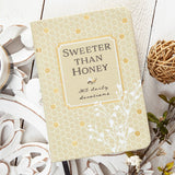 Book titled 'Sweeter Than Honey' on a decorative surface with plants and balls.