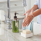 Person washing hands with soap and water in a kitchen sink.