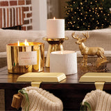 Decorative candles and a deer figurine on a table with a Christmas tree in the background.