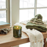 Green candle on a wooden surface with a knitted hat and scarf in the background