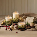 Candle holder with three lit candles on a wooden surface, surrounded by Christmas decorations.