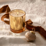 Candle in a decorative glass holder with a shell ornament on a textured surface