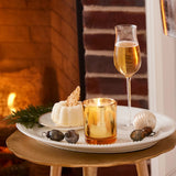 Glass of champagne and small dessert on a tray with a candle in front of a fireplace.