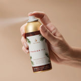 Hand holding a Thymes Frasier Fir home fragrance mist can against a beige background