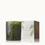 Green candle with embossed foliage design next to its packaging on a white background