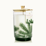 A candle with a gold lid and greenery design on a white background