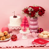 Decorative table setting with a cake, flowers, and pastries on a pink background