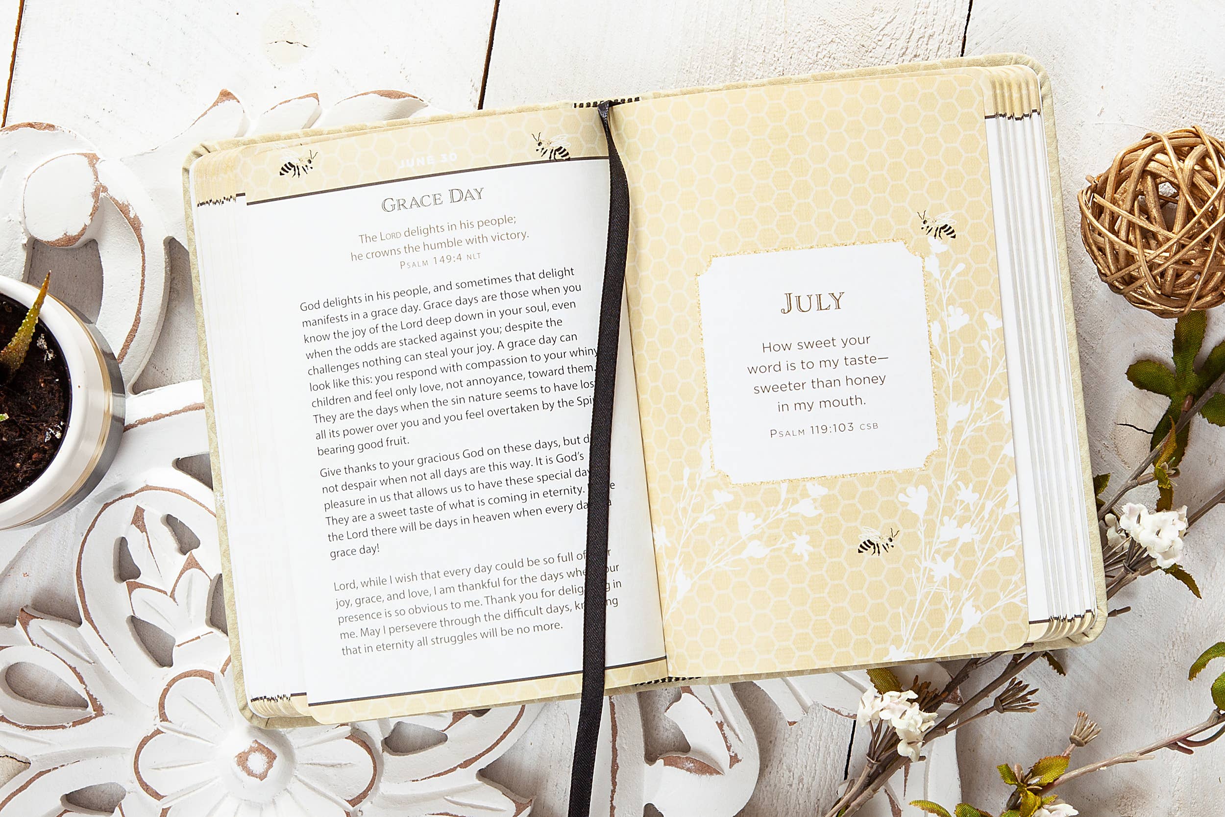 Open book with a page labeled 'July' on a decorative surface with plants and a cup.