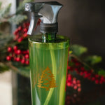 Green spray bottle with a logo on a reflective surface, blurred Christmas tree in the background