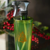 Green spray bottle with a logo on a reflective surface, blurred Christmas tree in the background