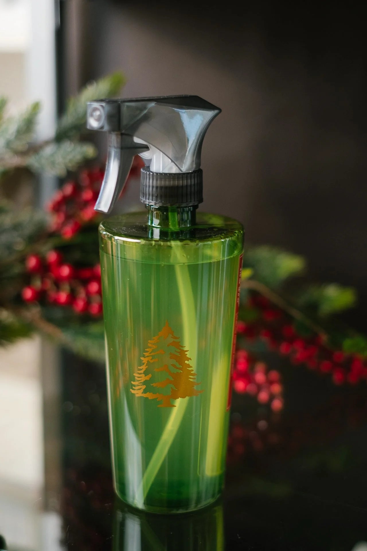 Green spray bottle with a logo on a reflective surface, blurred Christmas tree in the background