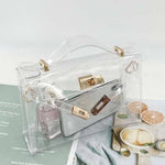 Clear handbag with gold accents on a surface with a magazine and food items.