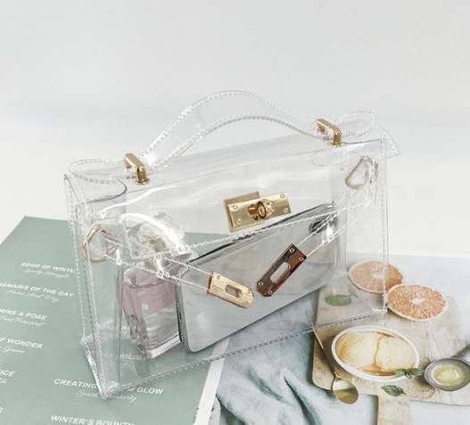 Clear handbag with gold accents on a surface with a magazine and food items.