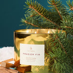 Gold candle labeled 'Frasier Fir' with pine branches on a blue background