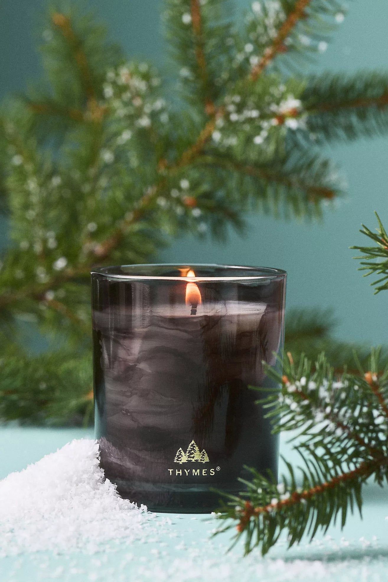 Thymes candle in a glass container with a Christmas tree branch in the background