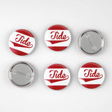 Six round pin-back buttons with a red and white striped design and the word 'Tide' in red script, shown on a light gray background with two front views and two back views.