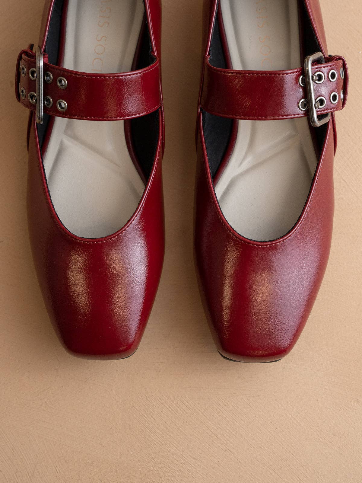 Pair of red shoes with buckles on a beige background