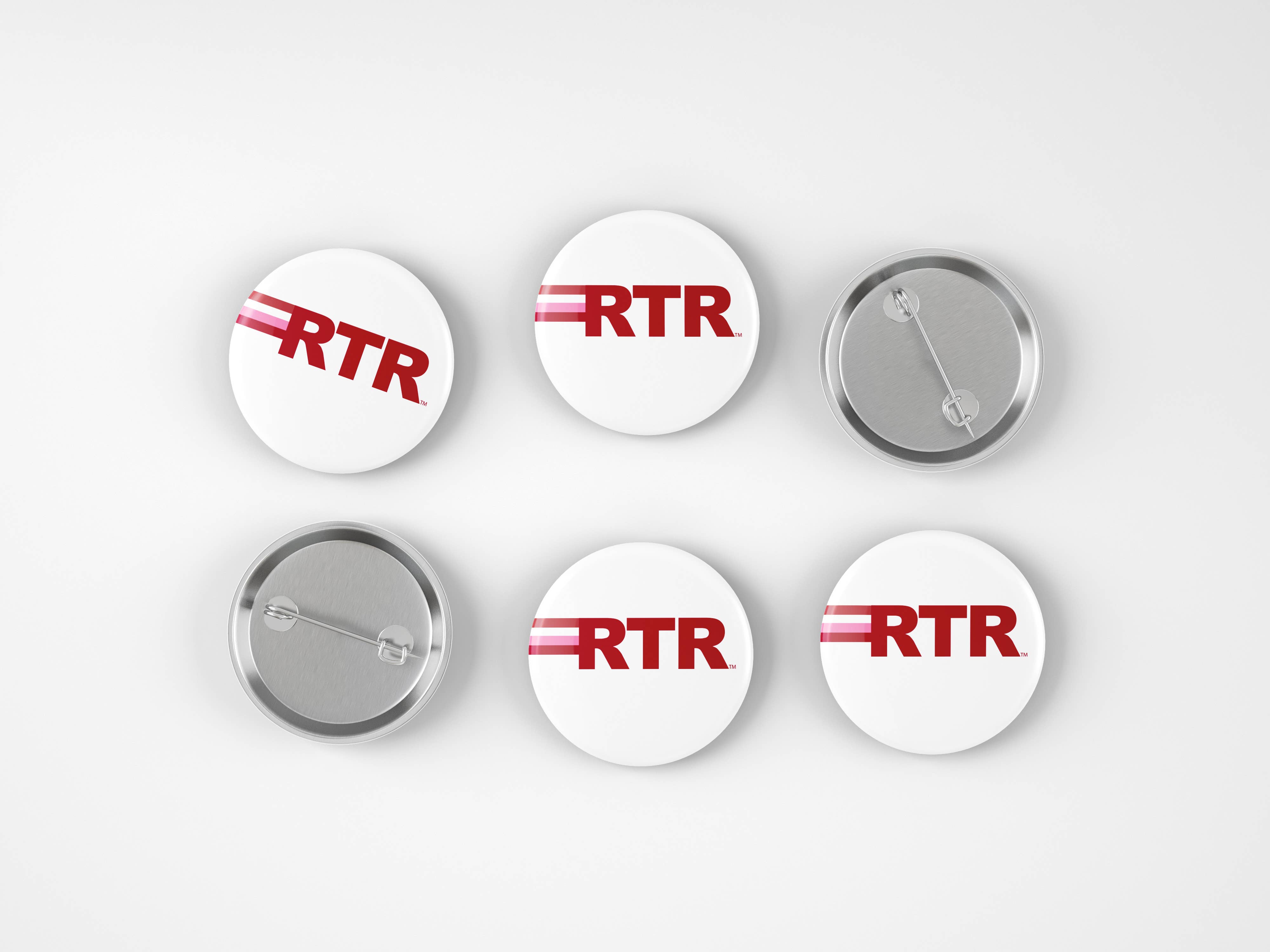 Six round pin-back buttons shown from front and back on a light gray background. The front buttons are white with red 'RTR' lettering and a thin red stripe, while the back buttons show the silver metal clasp.