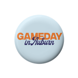 A round light blue button badge featuring the text 'GAMEDAY in Auburn' in orange and navy blue lettering, centered on a plain white background.