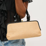 Beige handbag with black frame held by a person wearing a black top and blue jeans on a light gray background